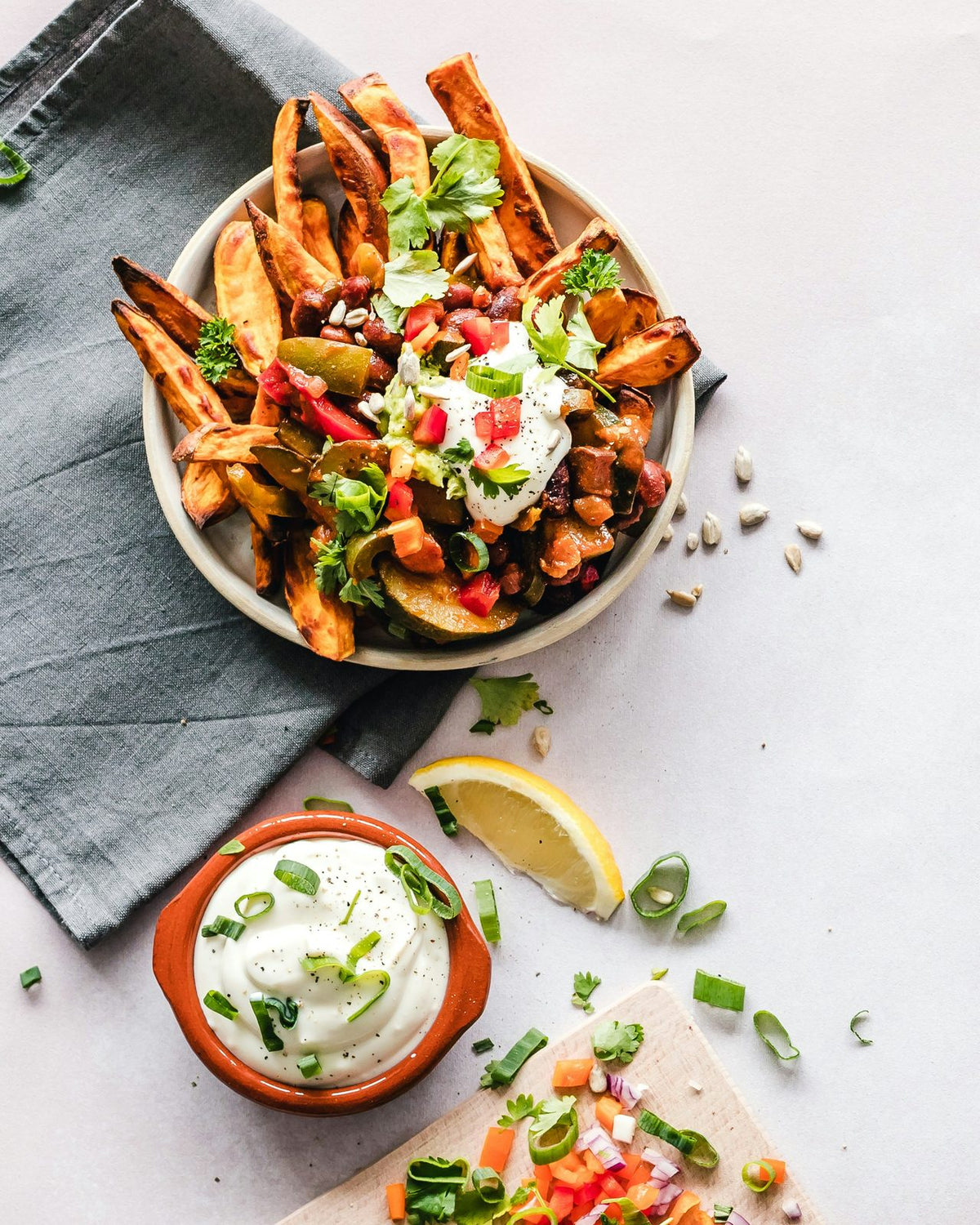 Bowl of loaded sweet potato wedges beside a terracotta bowl of creamy white dip scattered with green onion; better-than-the-tub chive and onion dip, ready for dunking