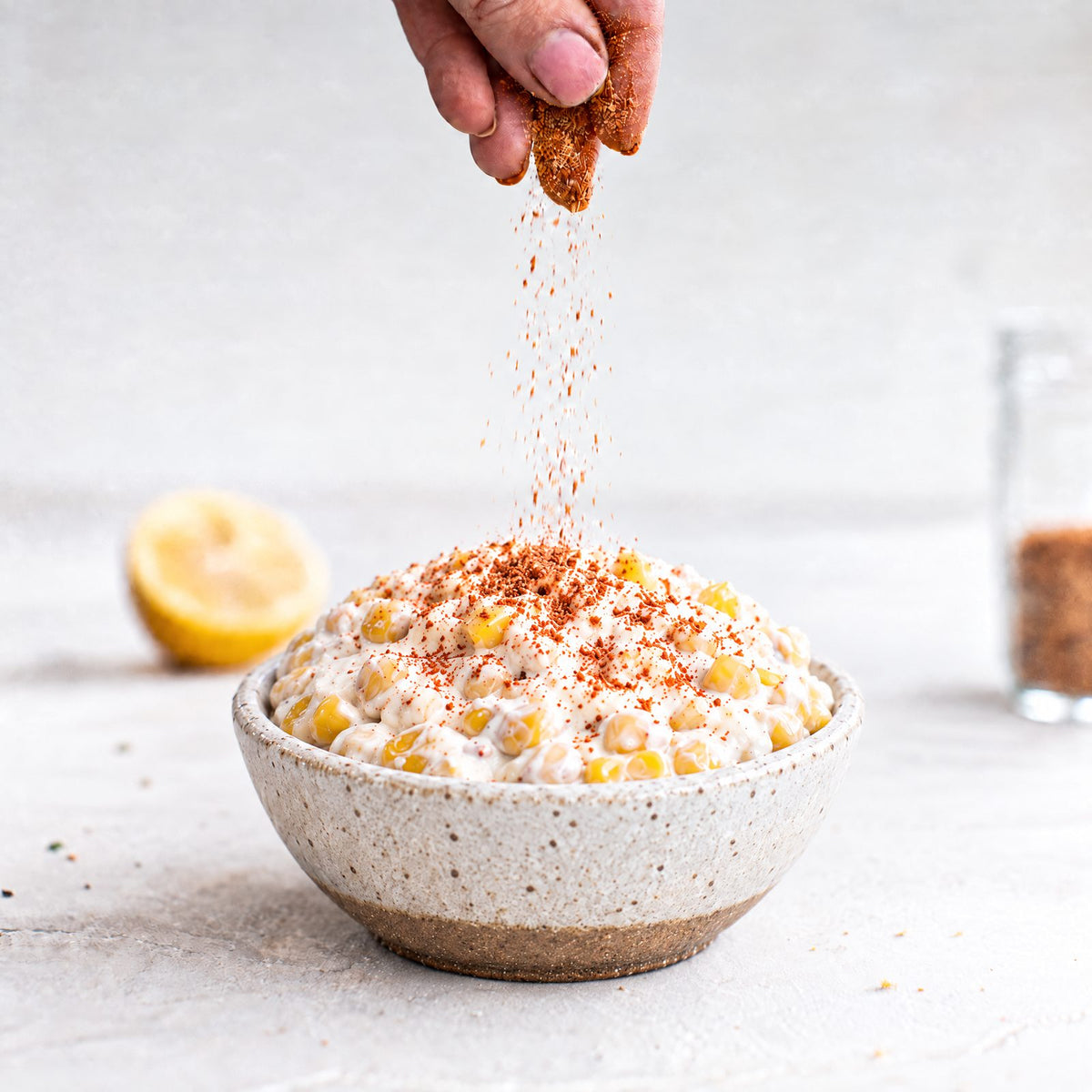 Corn and bacon dip made without bacon, being sprinkled with No-Bacon Bacon Salt in a speckled ceramic bowl