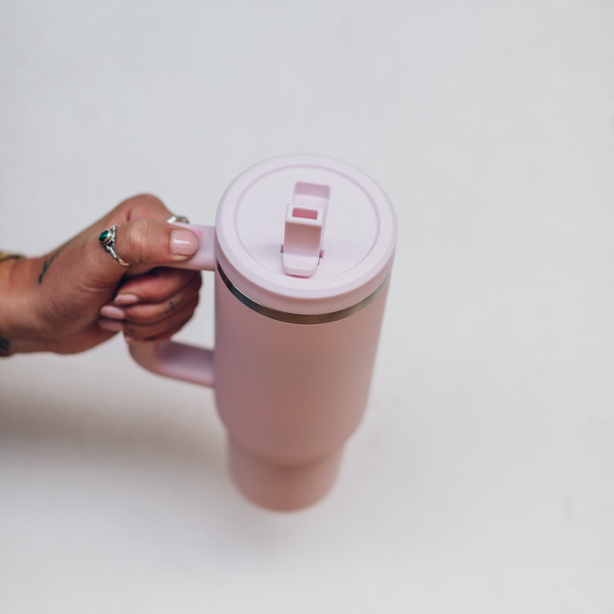 Blush pink 1L Insulated Tumbler held by the handle with the flip-top lid closed, shown from above