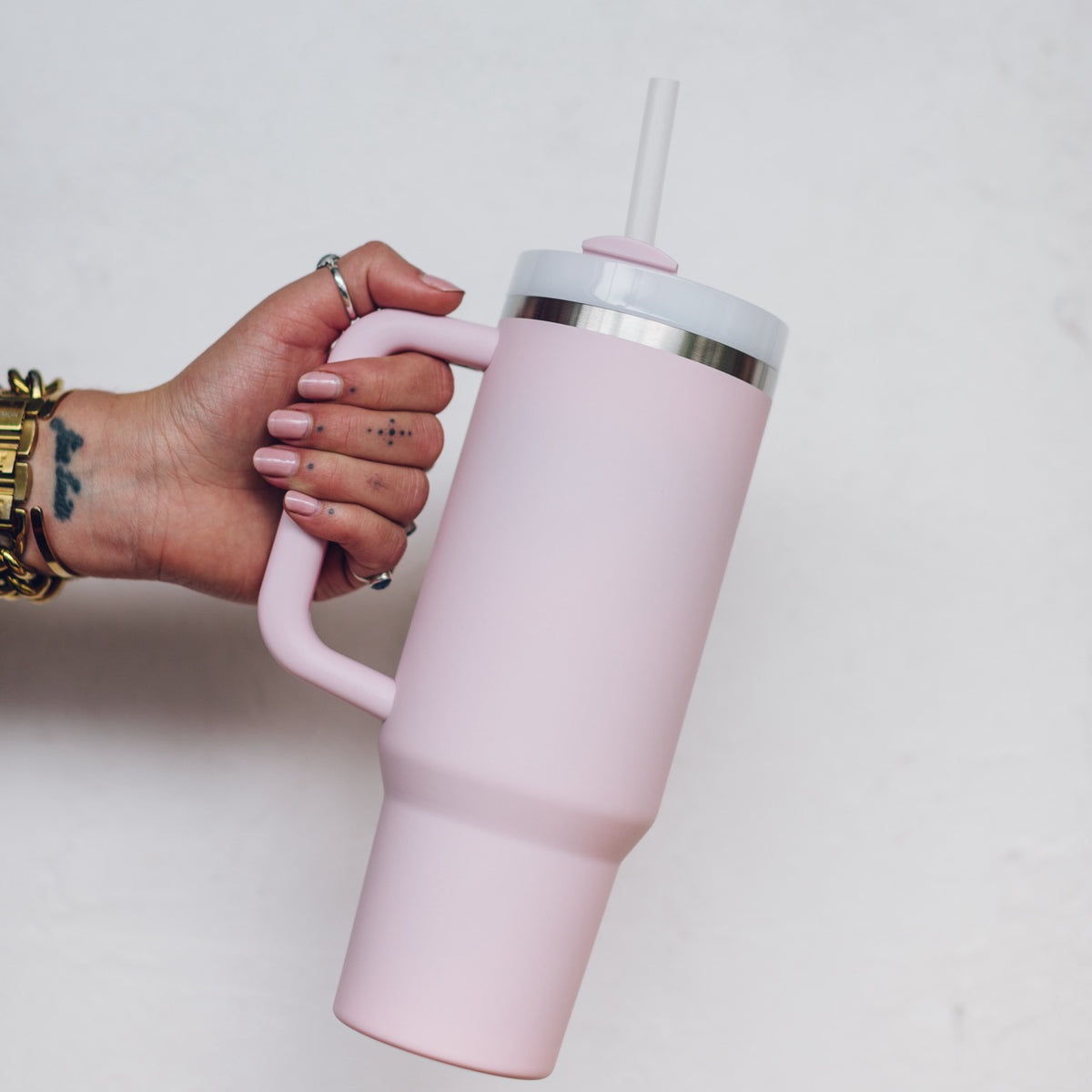 Blush pink 1L Insulated Tumbler held by its curved handle with the straw lid fitted, shown side on