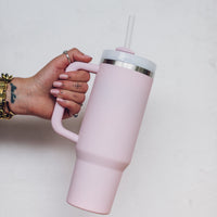 Blush pink 1L Insulated Tumbler held by its curved handle with the straw lid fitted, shown side on
