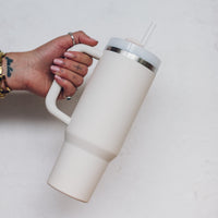 Cream 1L Insulated Tumbler held by the handle with the straw lid fitted