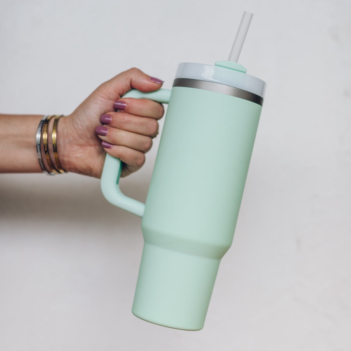 Sage green 1L Insulated Tumbler held by the handle with the straw lid fitted