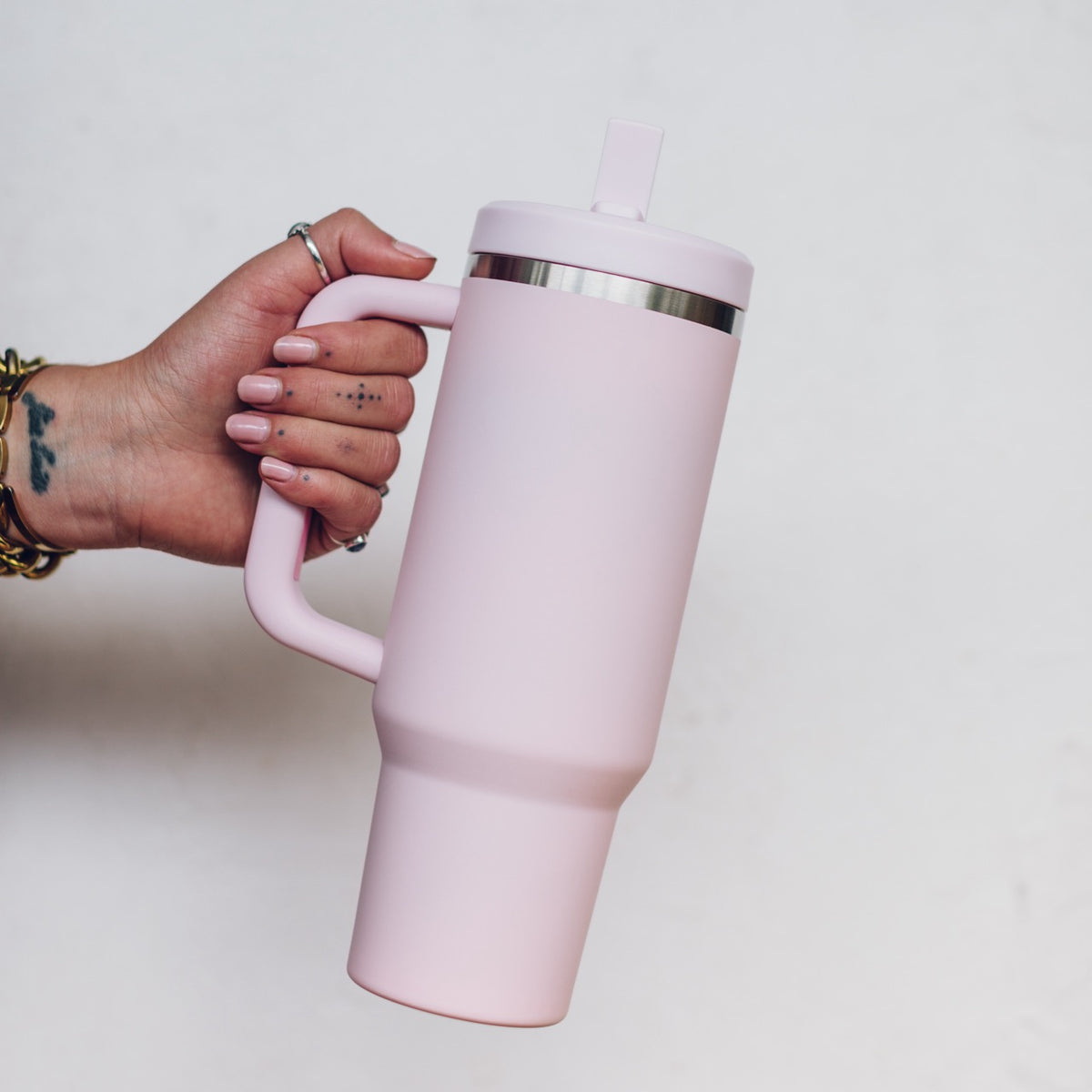 Pale pink 1L Insulated Tumbler held by the handle with the straw lid fitted, showing the tapered base