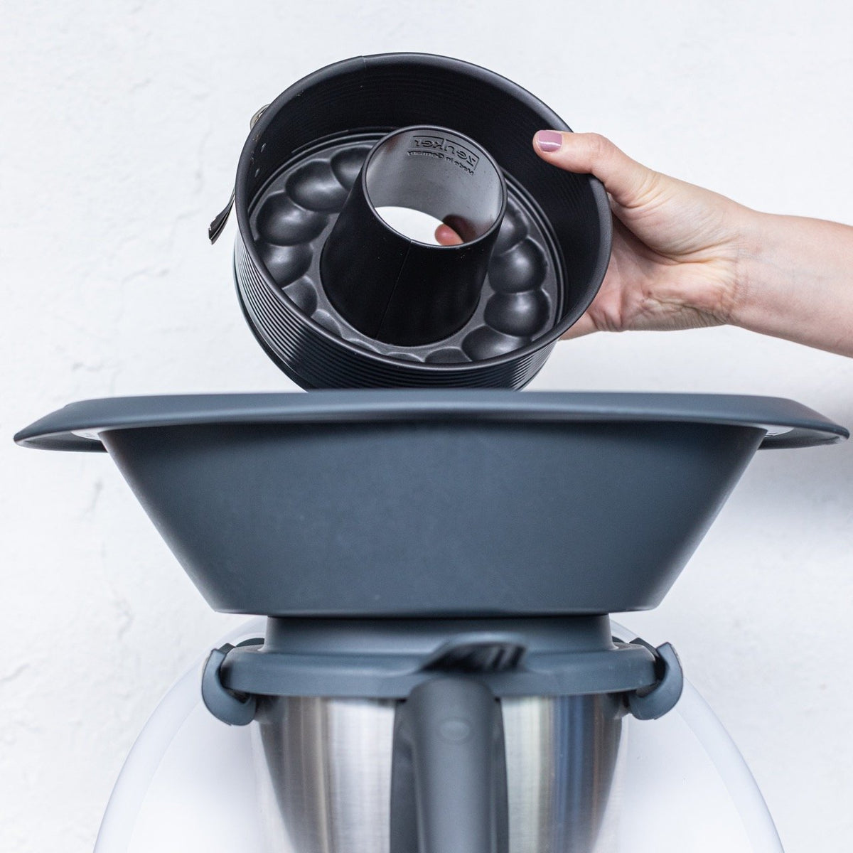 Hand holding the 2-in-1 Springform Pan above the Varoma of a Thermomix to show that it fits inside