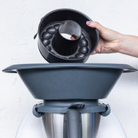 Hand holding the 2-in-1 Springform Pan above the Varoma of a Thermomix to show that it fits inside