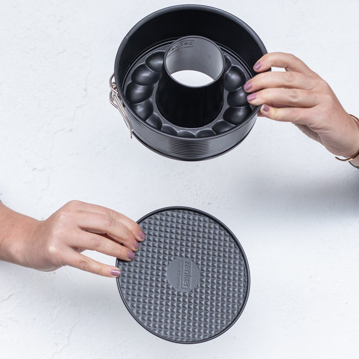 Hands lifting the 2-in-1 Springform Pan away from its textured silicone base to show the two parts separating