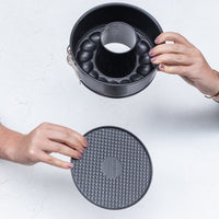 Hands lifting the 2-in-1 Springform Pan away from its textured silicone base to show the two parts separating