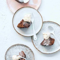 Two plates of steamed pudding served with cream, on a pale bench