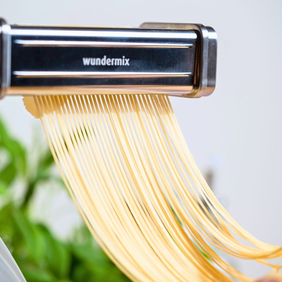 Close-up of fresh spaghetti falling from the cutter attachment in a neat curtain of strands