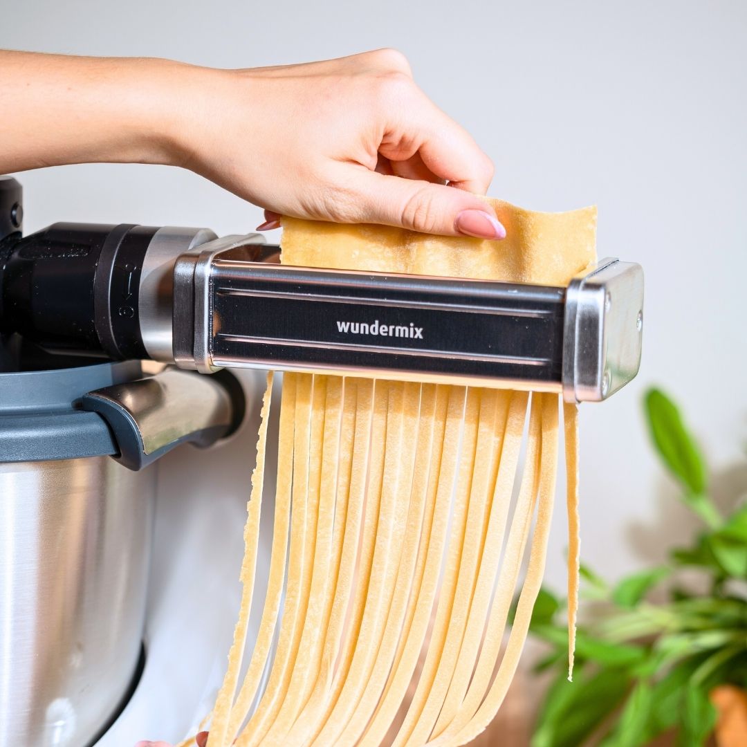 Hand feeding a sheet of pasta dough into the cutter while cut fettuccine falls from underneath