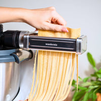 Hand feeding a sheet of pasta dough into the cutter while cut fettuccine falls from underneath