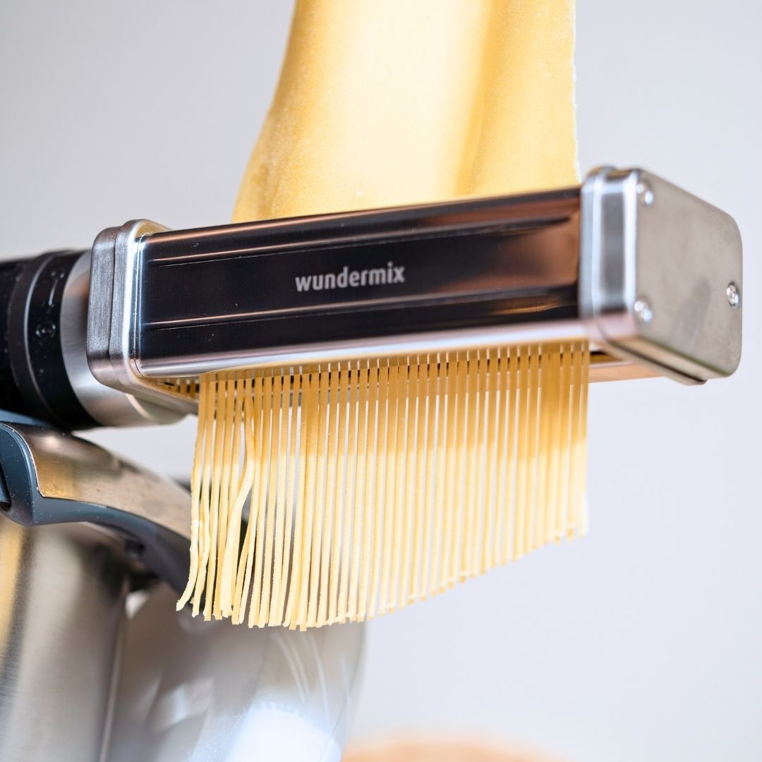 Fresh spaghetti hanging from the cutter attachment, shown close up against a pale background