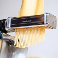 Fresh spaghetti hanging from the cutter attachment, shown close up against a pale background