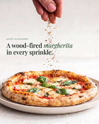 Hand sprinkling Instant Italian Salt over a wood-fired margherita pizza topped with mozzarella and fresh basil; a wood-fired margherita in every sprinkle
