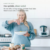 Alyce sprinkling Organic Flavour Bomb Salt over a bowl of pasta beside her Thermomix; one sprinkle and dinner is sorted, no new skills and no long recipes, season as you cook or finish at the table