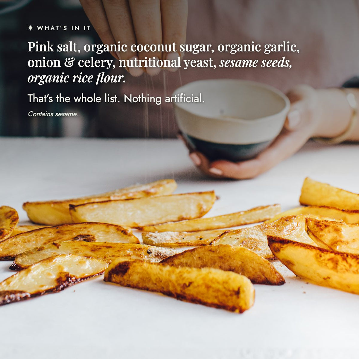 Hand holding a bowl beside a pile of golden chips; the whole ingredient list for No-Chicken Chicken Salt is pink salt, organic coconut sugar, organic garlic, onion and celery, nutritional yeast, sesame seeds and organic rice flour, nothing artificial, contains sesame