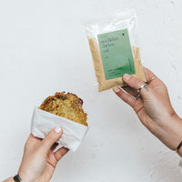 Hands holding a crispy golden hash brown wrapped in paper alongside a packet of No-Chicken Chicken Salt