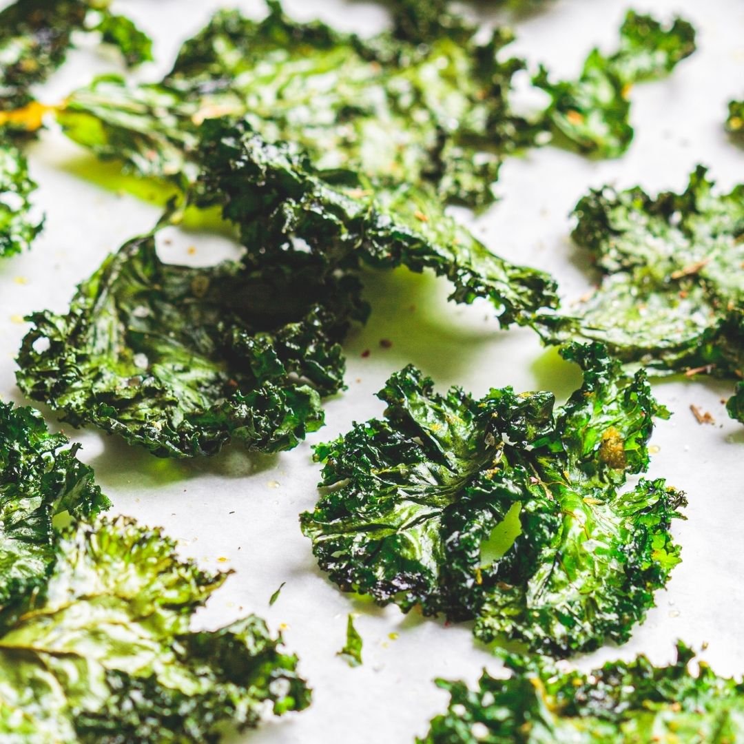 Crispy kale chips seasoned with No-Chicken Chicken Salt spread across baking paper