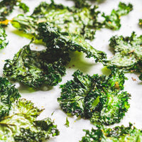 Crispy kale chips seasoned with No-Chicken Chicken Salt spread across baking paper