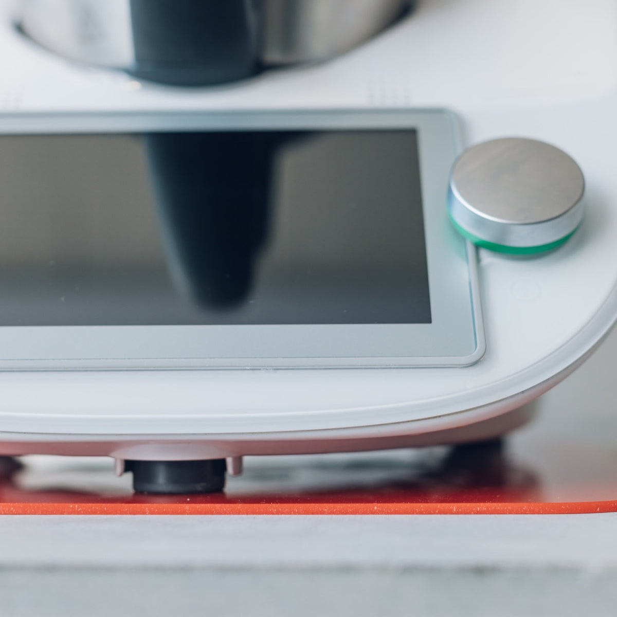 Close-up of a Thermomix base lifted slightly by a red Appliance Mat, showing the mat's low profile against the bench