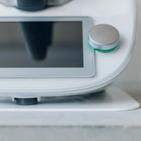 Close-up of a Thermomix base on a white Appliance Mat, showing the machine's feet resting on the mat