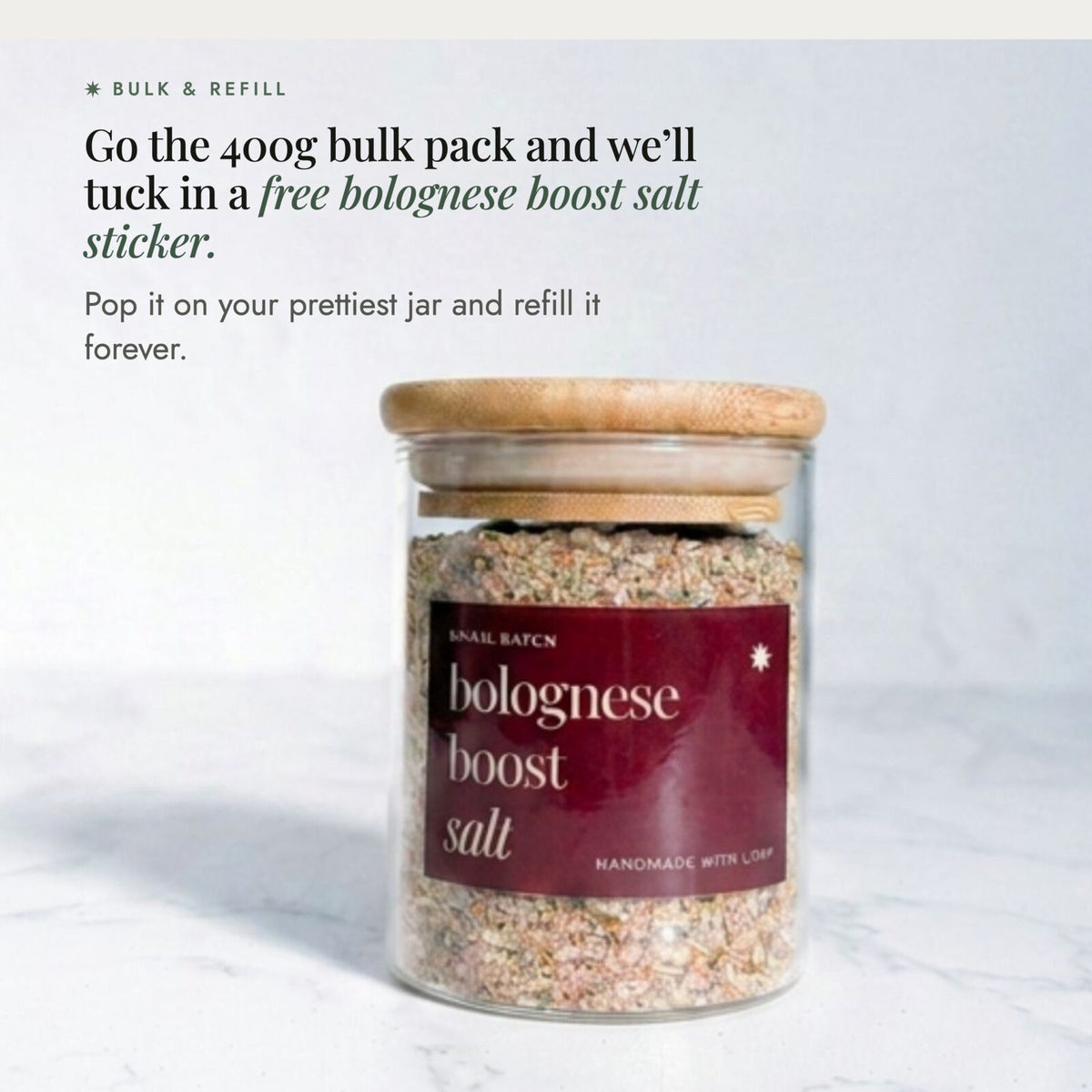 Glass jar of Bolognese Boost Salt with a bamboo lid on a marble bench; the 400g bulk pack includes a free sticker to pop on your own jar and refill forever
