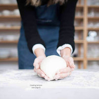 Hands shaping a round of bread dough on a floured bench, from the booklet's page on creating tension in the dough