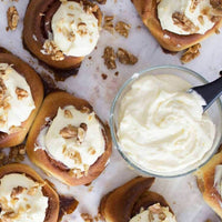Overhead tray of cinnamon scrolls topped with cream cheese icing and chopped walnuts, from the Bread Class Booklet