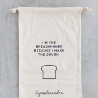 Breadwinner Bread Bag in natural organic cotton with a drawstring top, printed with a loaf illustration and the line I'm the breadwinner because I make the dough