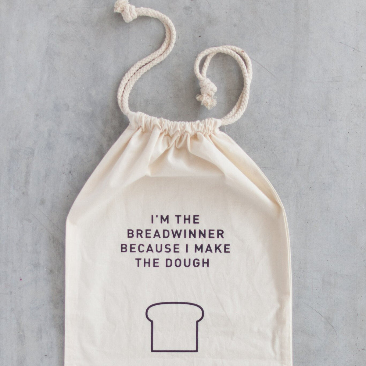 Breadwinner Bread Bag hanging with its drawstring pulled open, printed with the breadwinner slogan and loaf illustration