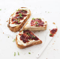 Slices of sourdough loaf of bread topped with cream cheese, jam and micro herbs on a white bench