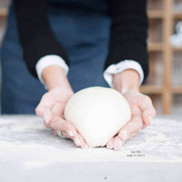 Hands shaping a round of dough on a floured bench, from the bap rolls recipe in the Champagne Breakfast Class Booklet