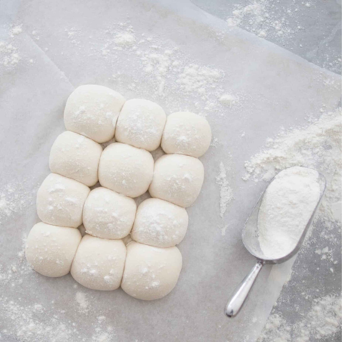 Tray of proved bap rolls dusted with flour beside a flour scoop, from the Champagne Breakfast Class Booklet
