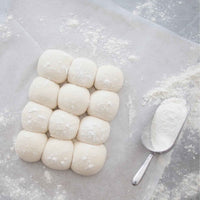 Tray of proved bap rolls dusted with flour beside a flour scoop, from the Champagne Breakfast Class Booklet