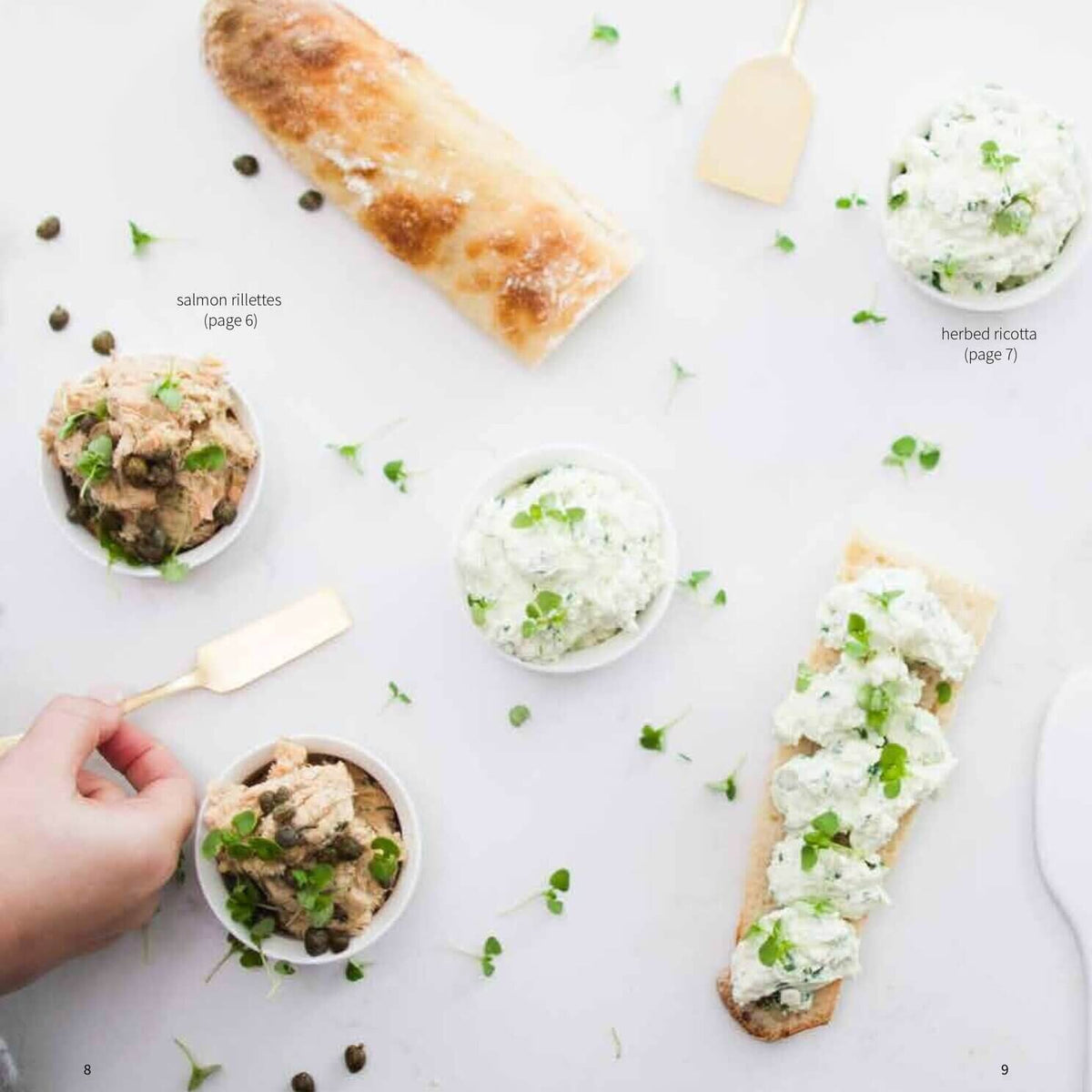 Hand spreading dip onto a baguette beside bowls of salmon rillettes and capsicum butter, from the Christmas Class Booklet