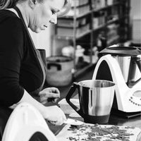 Black and white shot of Alyce teaching a live cooking class beside a Thermomix and its mixing bowl