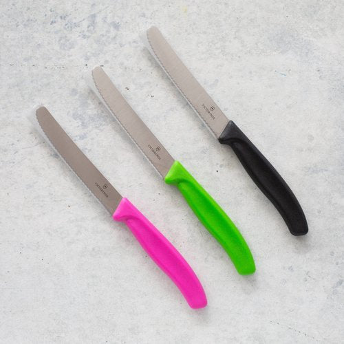 Four Classic Serrated Knives with pink, green, lilac and black handles laid on concrete