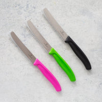 Four Classic Serrated Knives with pink, green, lilac and black handles laid on concrete
