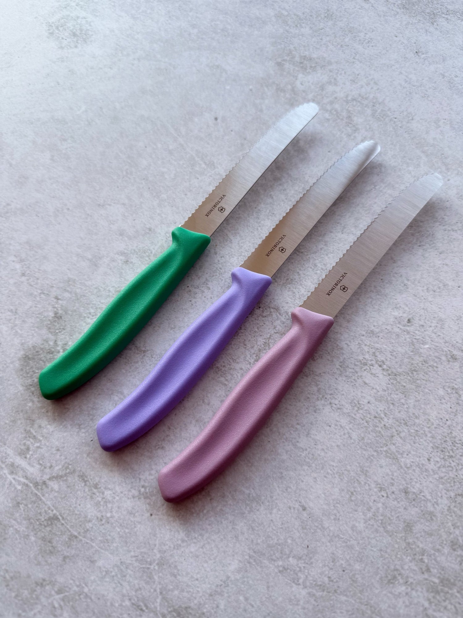 Four Classic Serrated Knives with green, lilac and pink handles fanned out