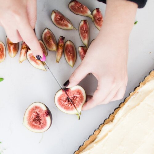 Hand using the Classic Serrated Knife to halve fresh figs on a tart
