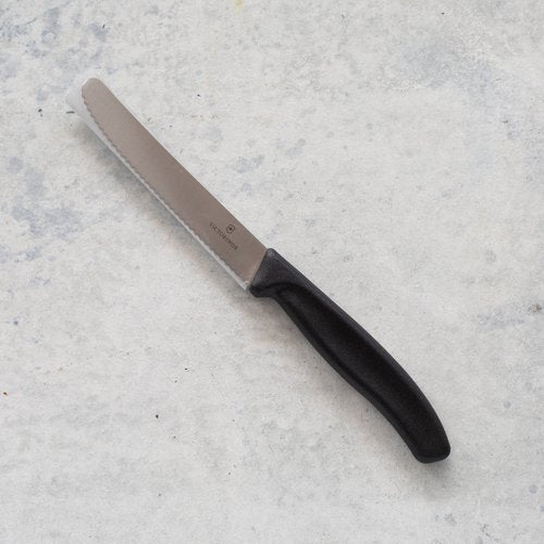 Classic Serrated Knife with a black handle laid on concrete