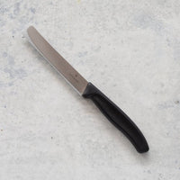 Classic Serrated Knife with a black handle laid on concrete