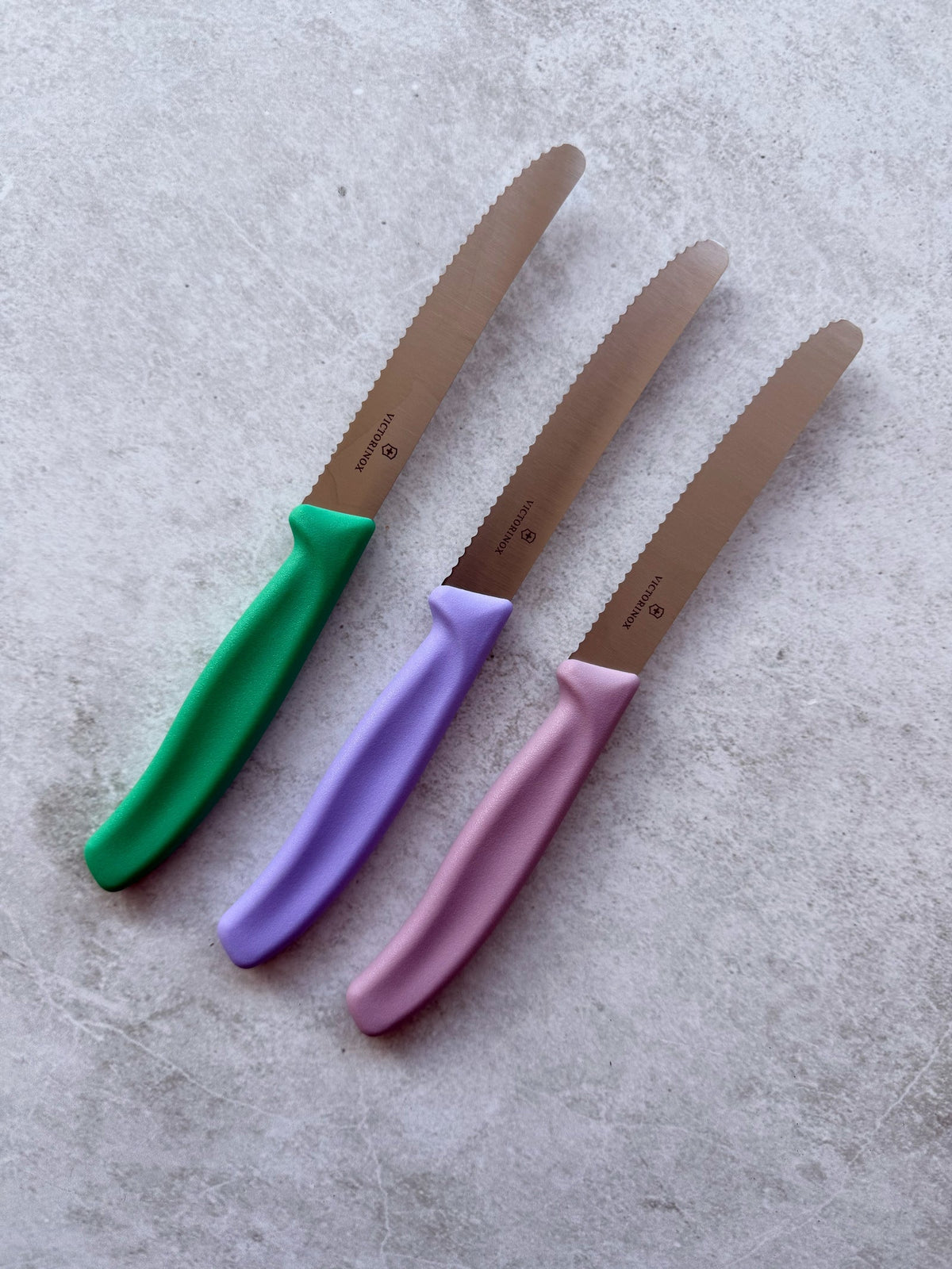 Three Classic Serrated Knives with green, lilac and pink handles arranged in a row