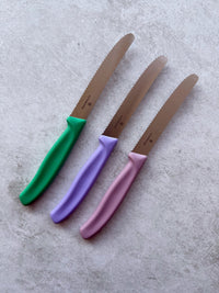 Three Classic Serrated Knives with green, lilac and pink handles arranged in a row