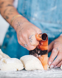 Tattooed hands using the Copper Dough Scraper to divide dough into portions on a floured bench
