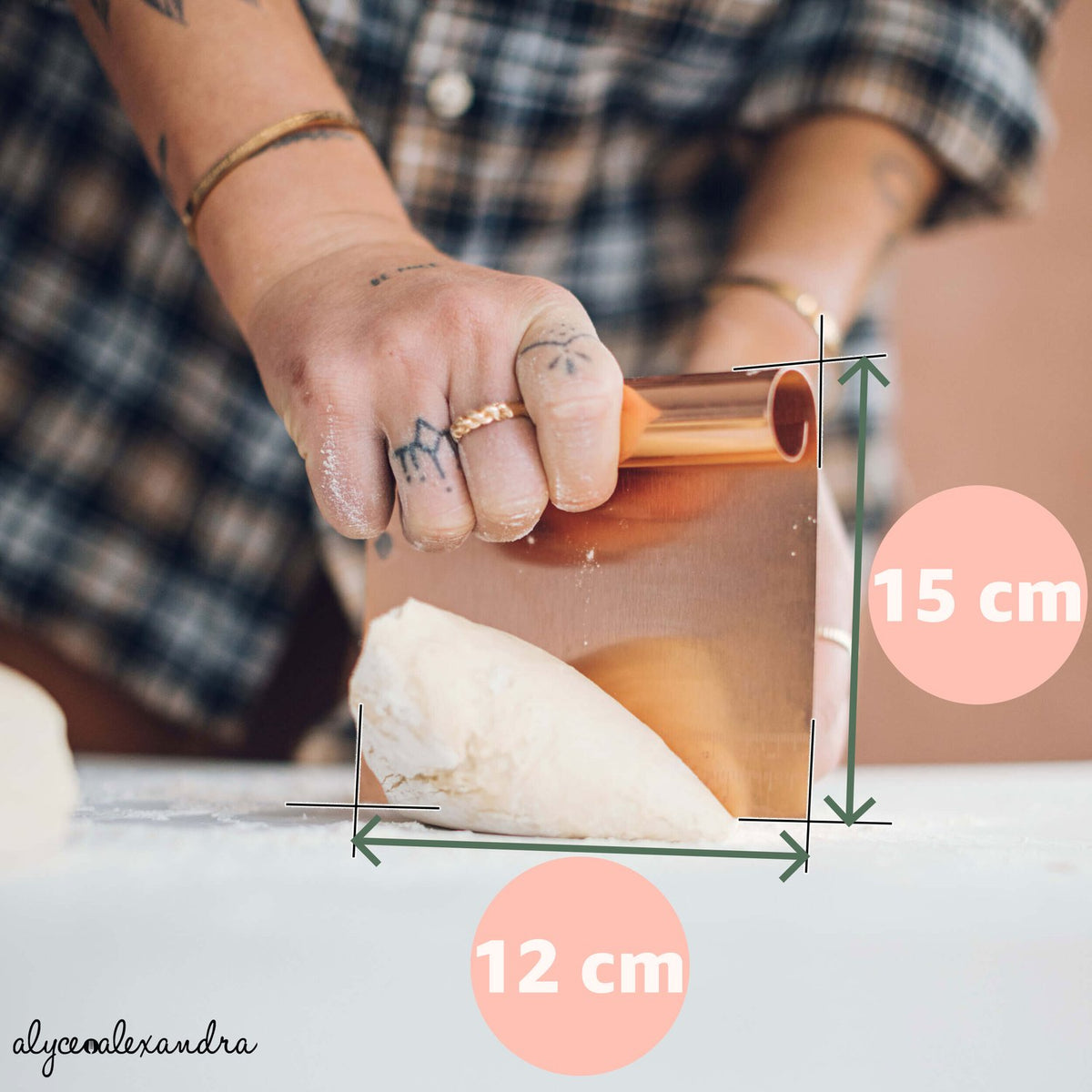 Copper Dough Scraper shown with its measurements, 15 cm tall and 12 cm wide, held against a round of dough