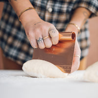 Copper Dough Scraper being pressed into a round of dough on a floured bench