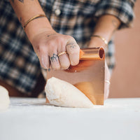 Close-up of the Copper Dough Scraper's copper handle and blade resting beside a round of dough