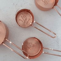 Copper Measuring Cups laid on a pale bench showing the embossed measurement markings inside each cup